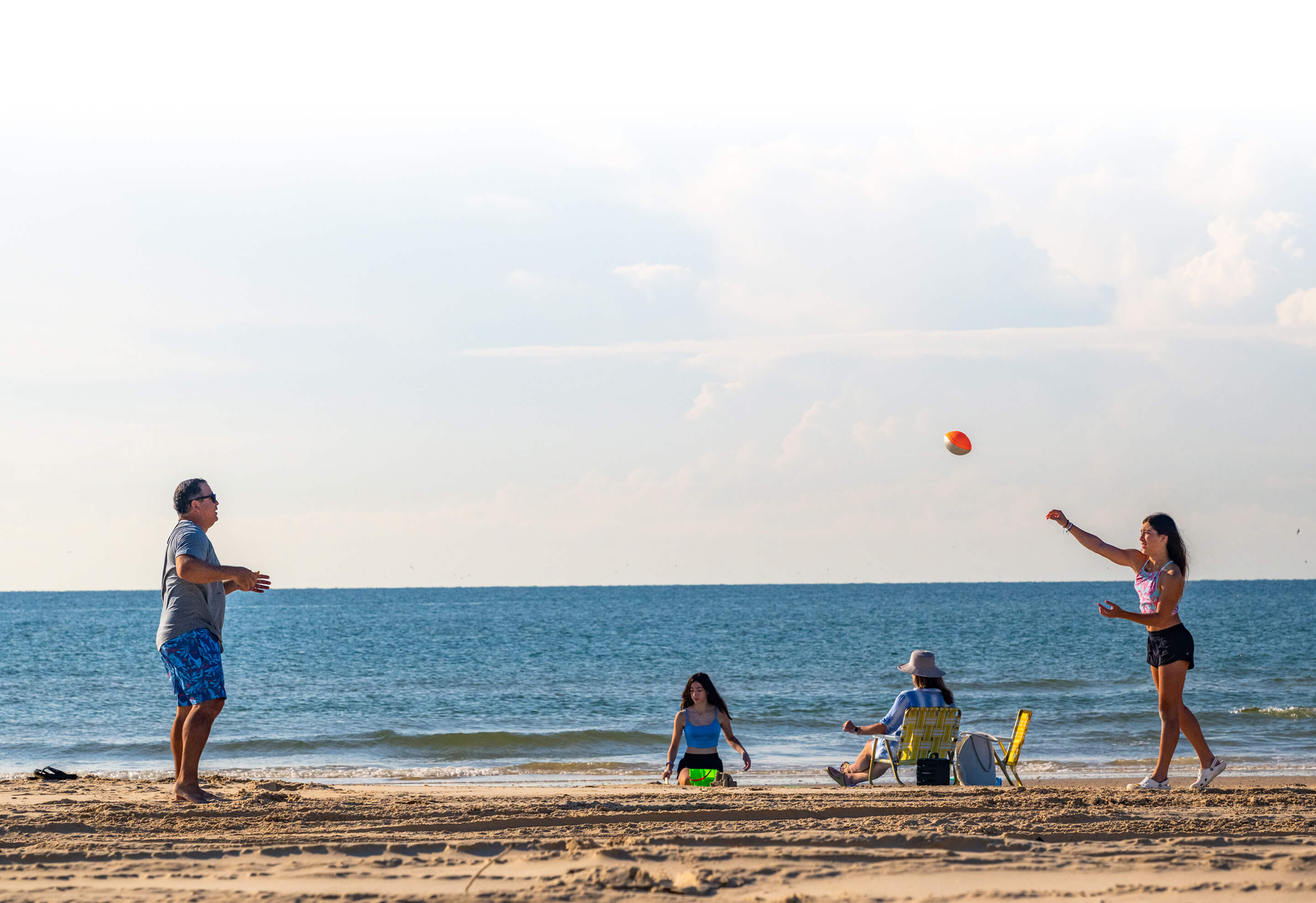 A beach scene showing a family throwing a ball to each other
